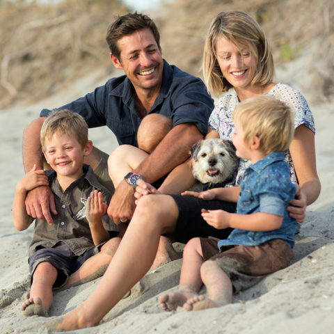 Family of four at the beach, sharing a happy moment together while sitting on a sand hill with their dog