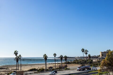 Exterior shot from balcony overlooking highway, coastline, and pier with tropical landscaping