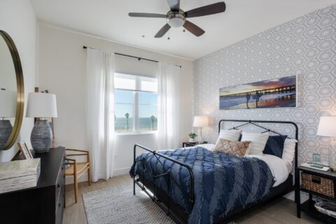 Bedroom with hardwood-style floors, accent colored walls, ceiling fan, lamps, and window