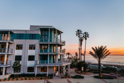 Outside view of apartment complex with sunset, palm trees, garden area, and ocean